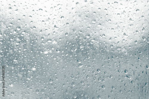 Raindrops on glass on the background of mosquito nets. Autumn wet rainy season.