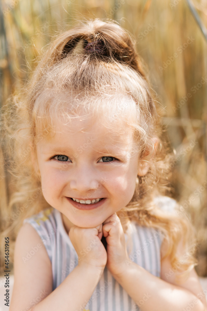 Close-up portrait of a smiling little girl blonde in nature in the summer