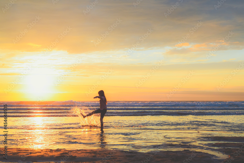 A girl stands at the shore of the ocean school age child playing and splashing sea water at the beach