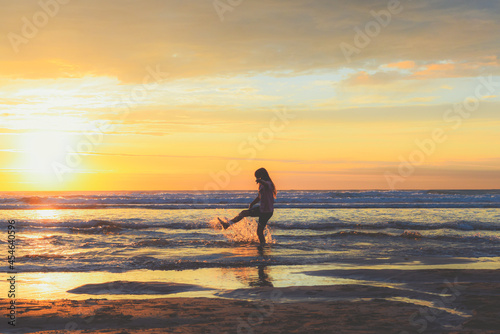A girl stands at the shore of the ocean school age child playing and splashing sea water at the beach