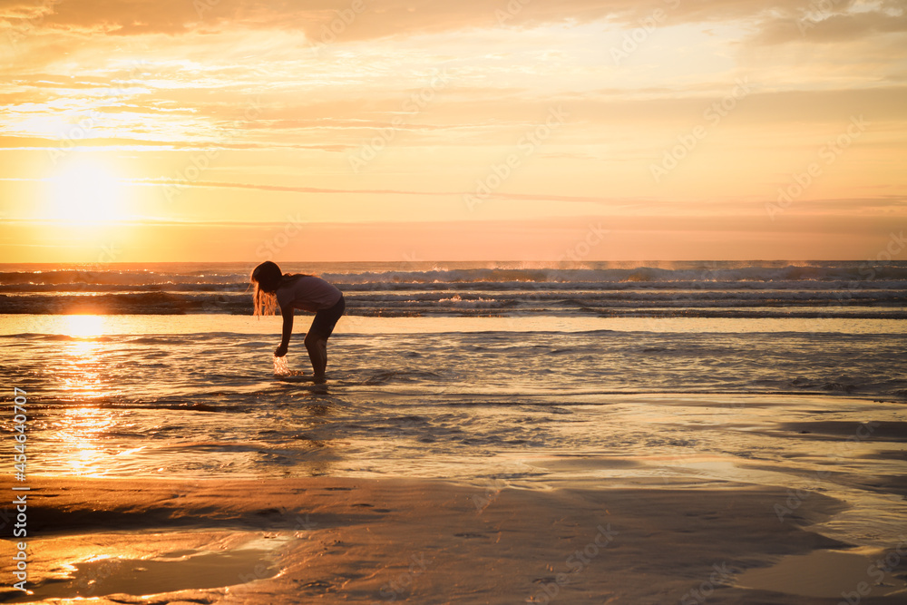 A girl stands at the shore of the ocean school age child playing and splashing sea water at the beach