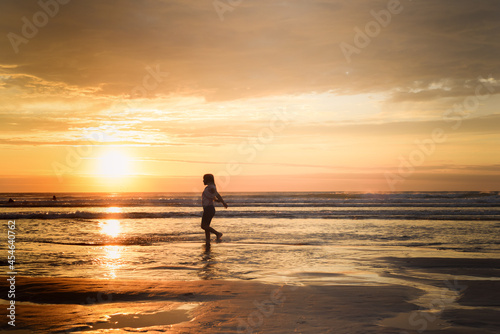 A girl stands at the shore of the ocean school age child playing and splashing sea water at the beach © tommoh29