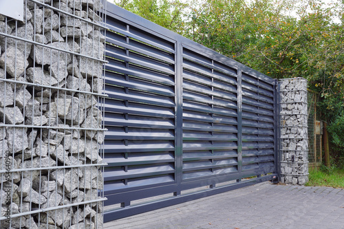 Gabion. Automatic entrance gate used in combination with a wall made of gabion.