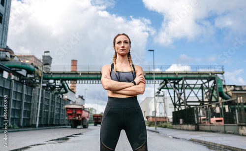 Sporty woman with crossed arms posing in front of a factory in an industrial zone