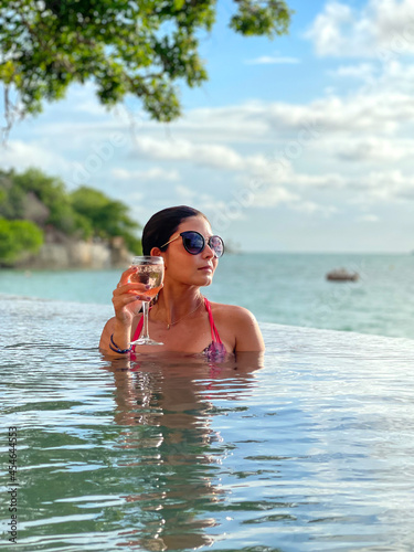 Portrait of a beautiful model woman celebrating with a cocktail in a paradise beach with sunglasses