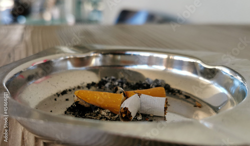 Portacenere in metallo lucido con sigaretta spezzata sul tavolino in legno marrone di un bar photo