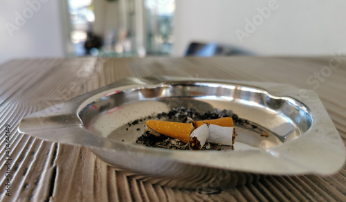 Portacenere in metallo lucido con sigaretta spezzata sul tavolino in legno marrone di un bar photo