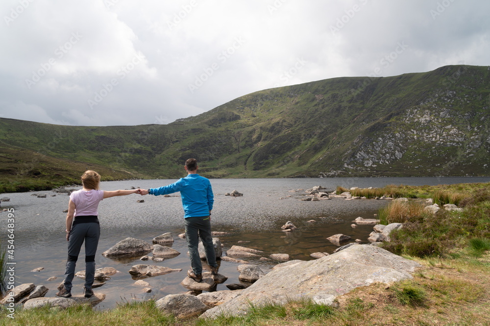Couple standing on a rock overseeing a beautiful blue waters of an Irish mountain. Holding hands.