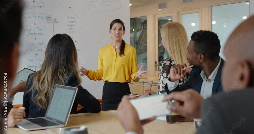 business woman leader meeting corporate team in office presenting ideas pointing at whiteboard discussing strategy with colleagues in boardroom presentation