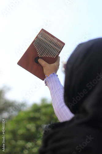 Photo Back pose Muslimah or Islam Girl Hold Kalimba, acoustic music instrument from africa 