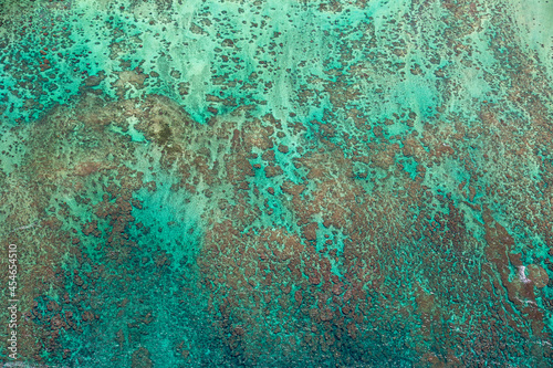 Abstract aerial view of coral reef in Oahu, Hawaii. Water has blue and green shades, reef is brown.