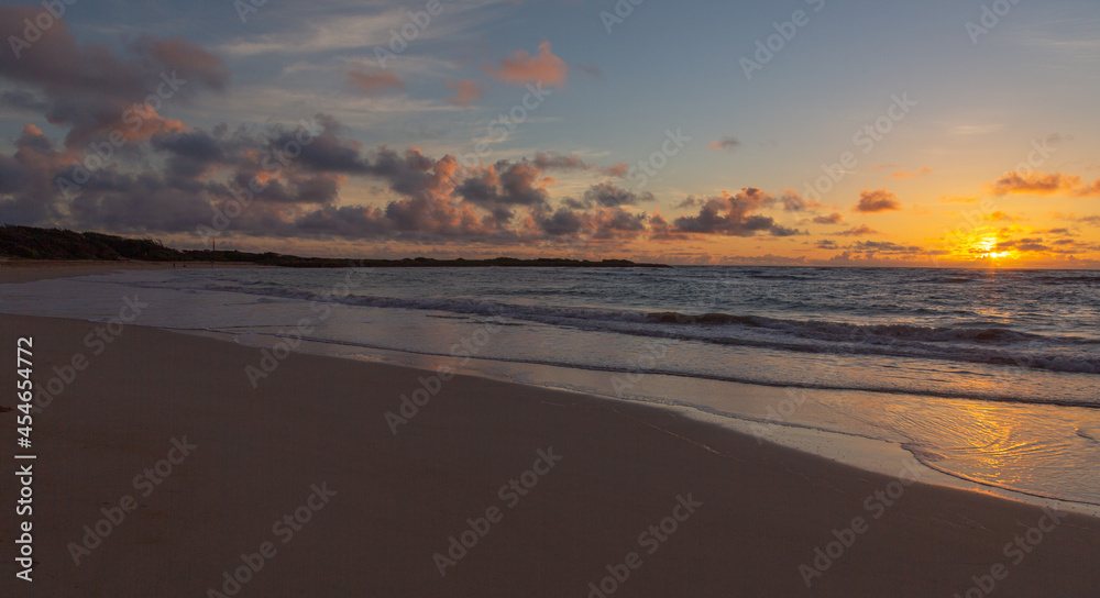 Hawaiian beach sunrise. Yellow, orange, and lavender hues in the sky, light cumulus clouds. 