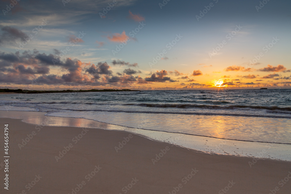 Hawaiian beach sunrise. Yellow, orange, and lavender hues in the sky, light cumulus clouds. 