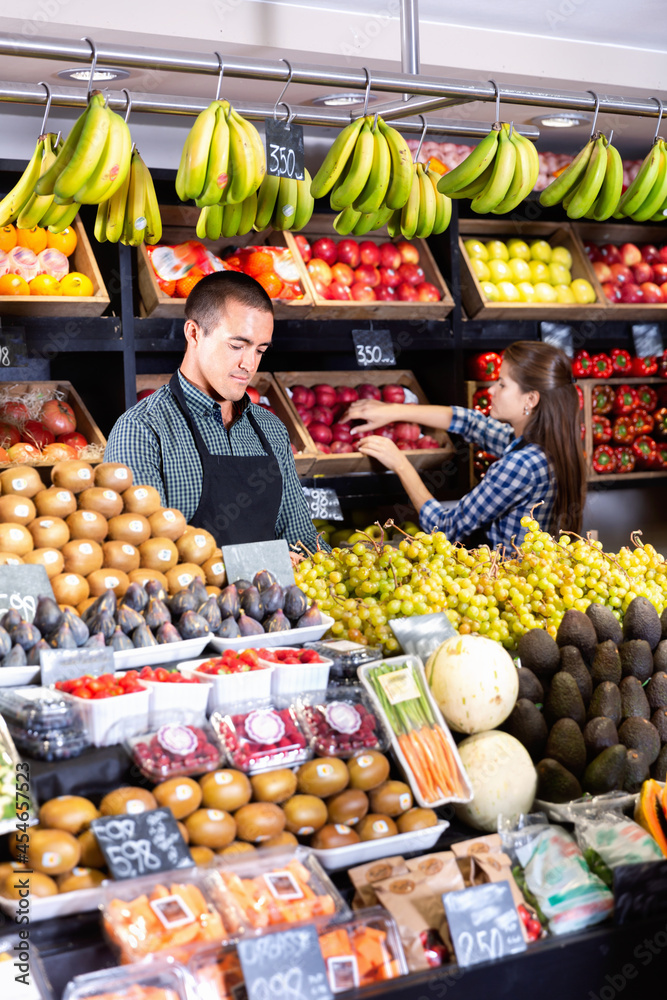 Friendly positive smiling man and woman laying out vegetables and fruits in shop