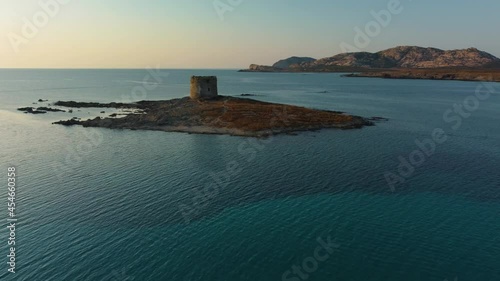 Aerial of La Pelosa, a famous natural sand beach sandy bay on the tourist holiday island Sardinia in Italy by sunset with clear blue turquoise water and a lighthouse watchtower. Drone air view flight.