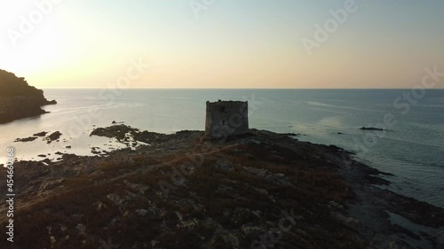 La Pelosa, a famous natural sand beach sandy bay on the tourist vacation island Sardinia in Italy by sunset with clear blue turquoise water and a lighthouse watchtower. Aerial drone air view flight.