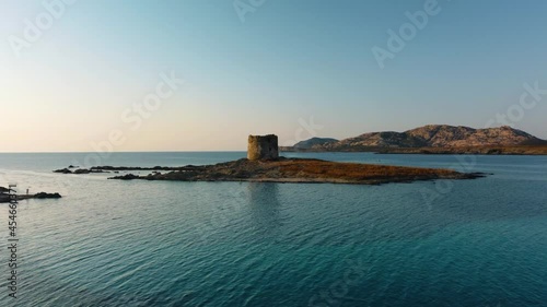 La Pelosa, a famous natural sand beach sandy bay on the tourist vacation island Sardinia in Italy by sunset, clear blue turquoise water with a lighthouse watchtower. Aerial drone air view flight.