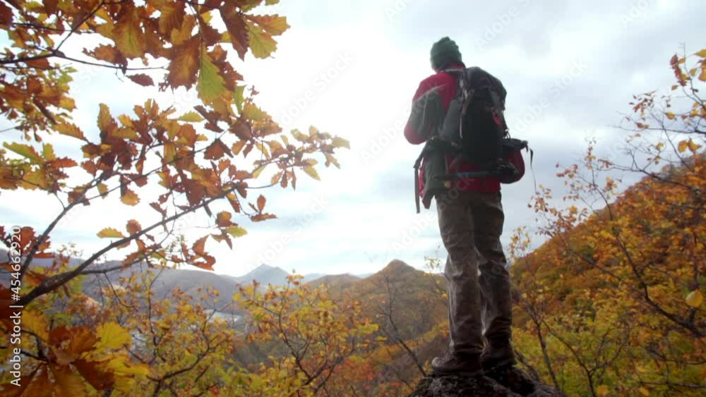 Back of a photographer standing on a high rock and taking pictures of a small city situated below in a valley between mountains. Autumn Back of a photographer standing on a high rock and taking pictures of a small city situated below in a valley between mountains. Autumn
