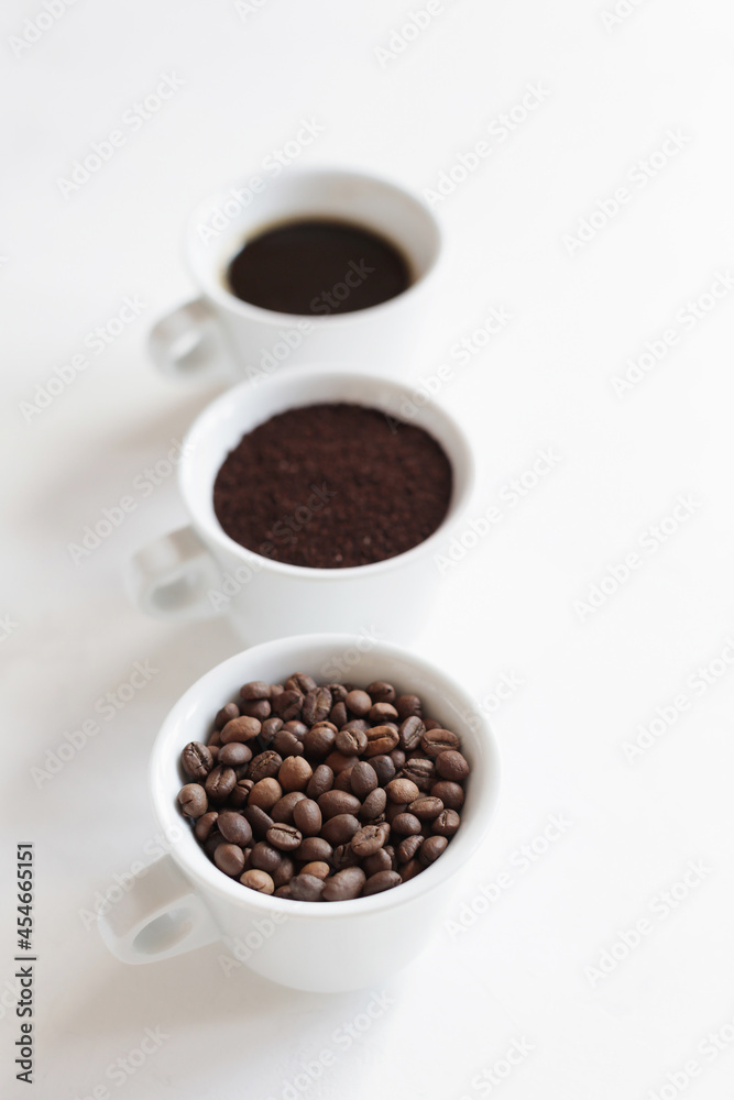 Fototapeta premium Assorted coffee in white cups, coffee beans, ground and black brewed. White background, copy space. Concept
