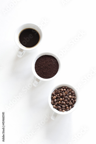 Assorted coffee in white cups, coffee beans, ground and black brewed. White background, copy space. Top view, Concept