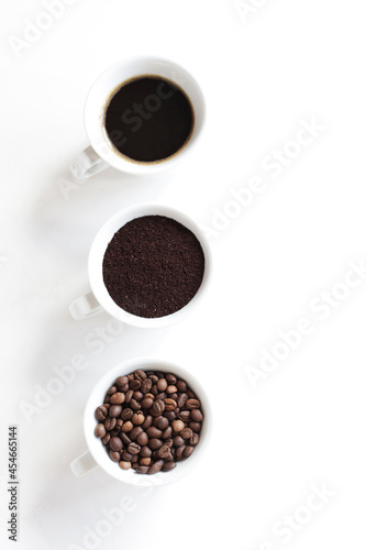 Top view, light background with white cups filled with assorted coffee, coffee beans, ground and black brewed.