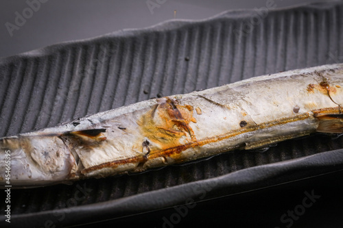 黒バックで黒いお皿に乗った焼いた秋刀魚のアップ　fish black