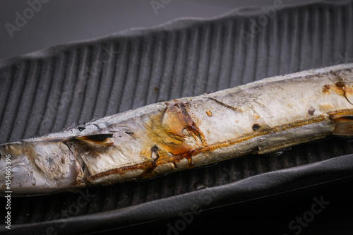 黒バックで黒いお皿に乗った焼いた秋刀魚のアップ　fish black