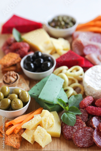 Large wooden board for snacks with different cheeses, meats, sausages, olives, nuts. Nice serving board with meats and cheeses. Vertical on a light background. Close-up