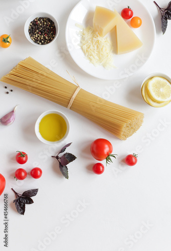 Food ingredients for Italian pasta, spaghetti, fresh farm tomatoes, garlic, peppers, basil, olive oil, Parmesan cheese, lemon, vegetable milk. On white background. Top view with copy space.
