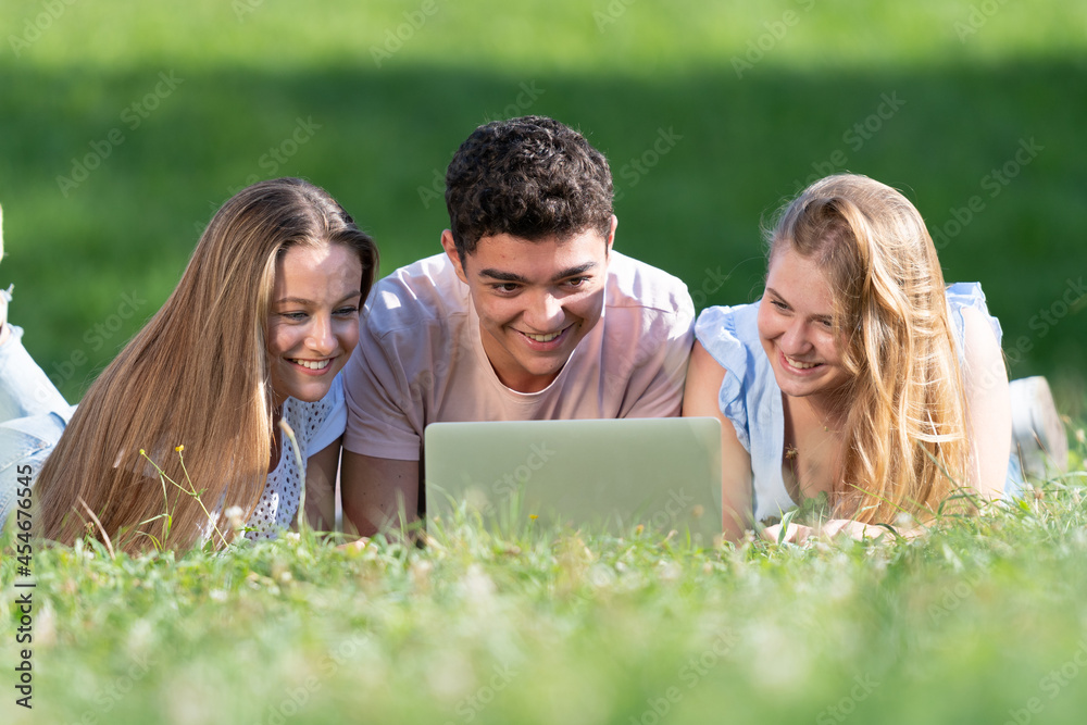 Multiethnic students working together on a laptop laying on the ground. Teamwork in adolescence age concept. Multiethnic students working together on a laptop laying on the ground. Teamwork in adolescence age concept.