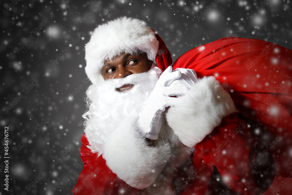 African-American Santa Claus with bag full of gifts on dark background African-American Santa Claus with bag full of gifts on dark background