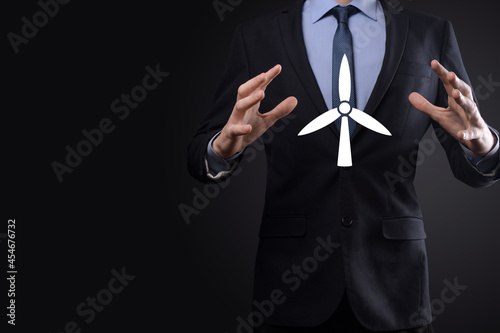 Businessman holding an icon of a windmill that produces environmental energy. Dark background