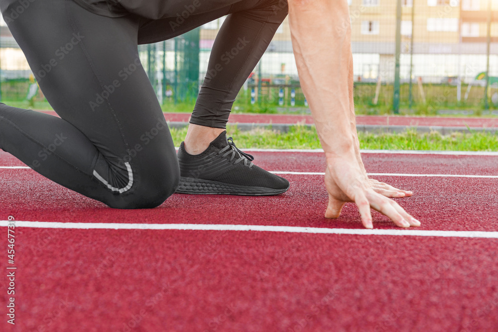 Athlete on the starting line of a stadium track preparing for a run.