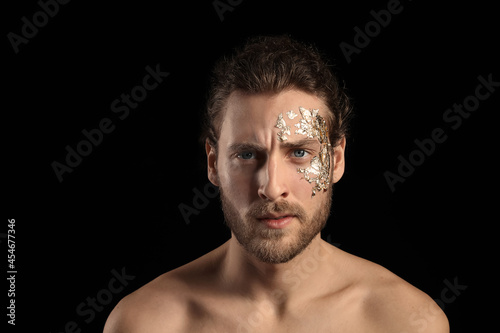 Handsome young man with golden foil on face against black background