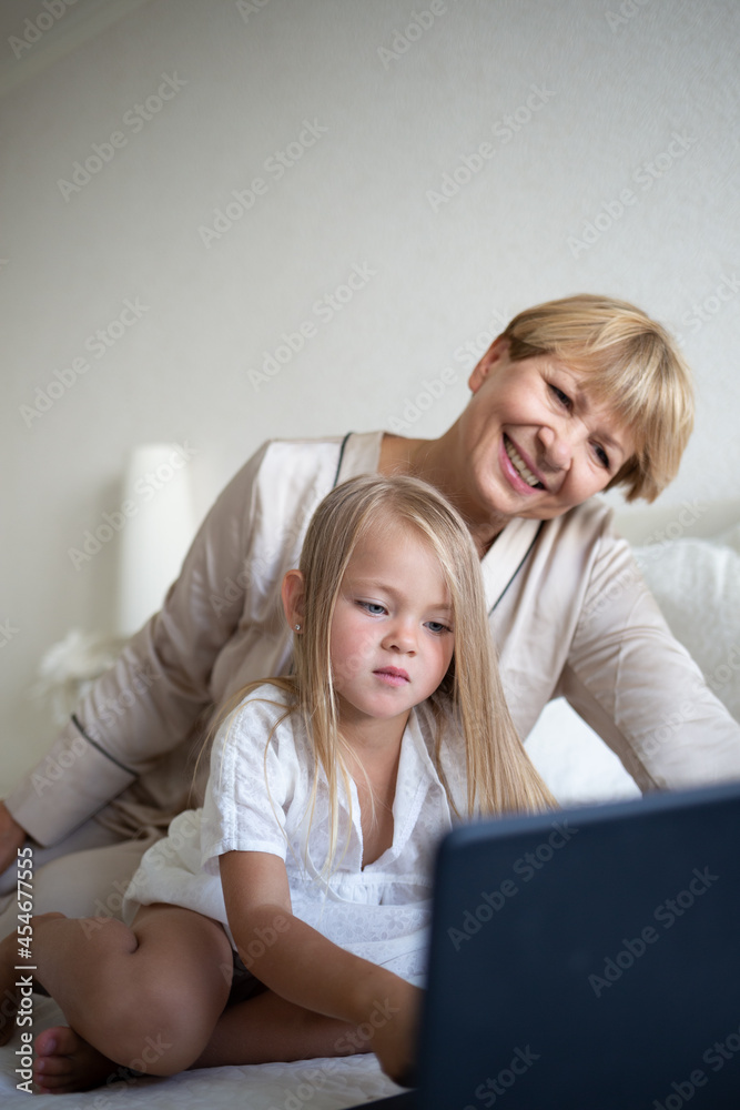 little girl with her grandmother sitting on the bed in front of a laptop little girl with her grandmother sitting on the bed in front of a laptop