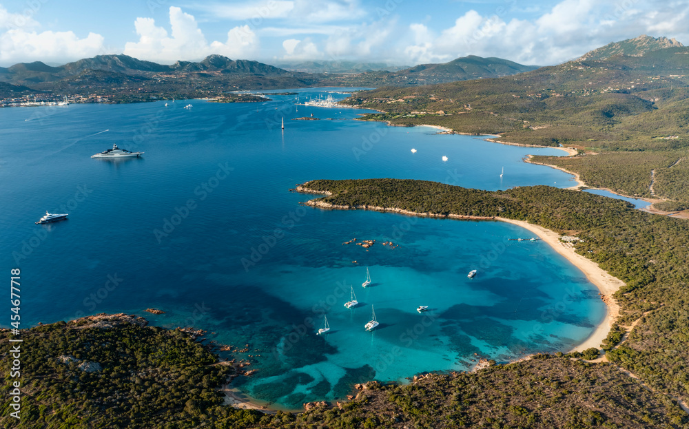 View from above, stunning aerial view of a green coastline with a white sand beach and and boats sailing on a turquoise water at sunset. Cala di volpe beach,Sardinia, Italy.