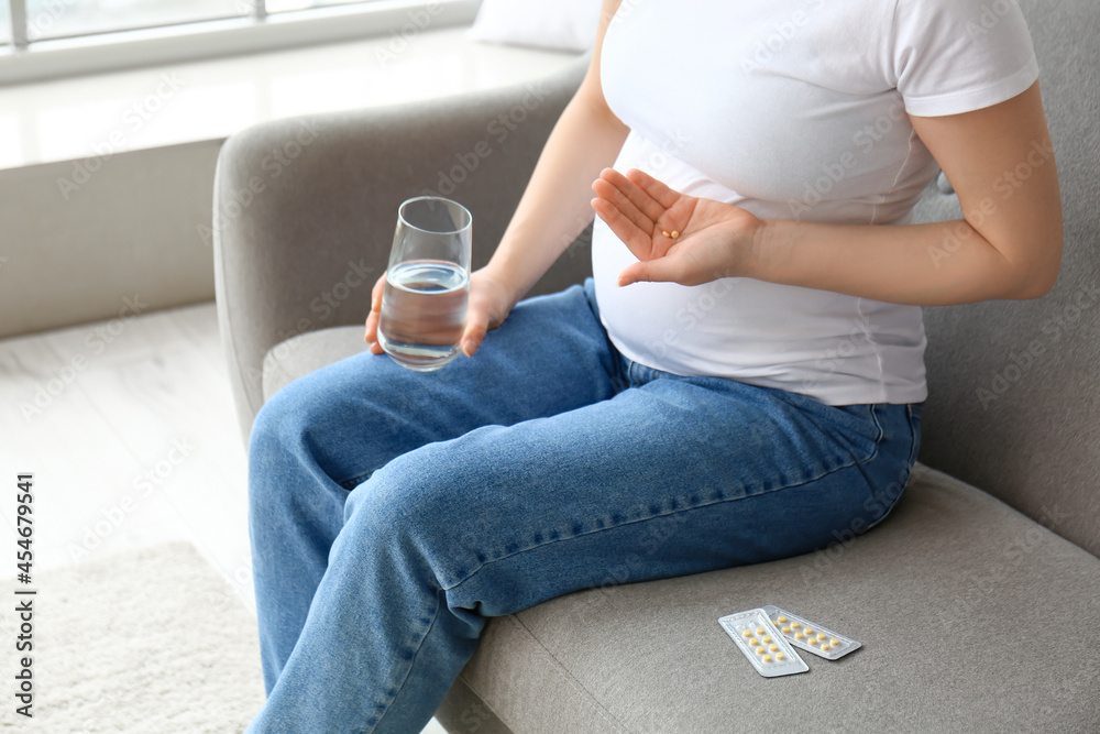 Young pregnant woman with pills and glass of water at home