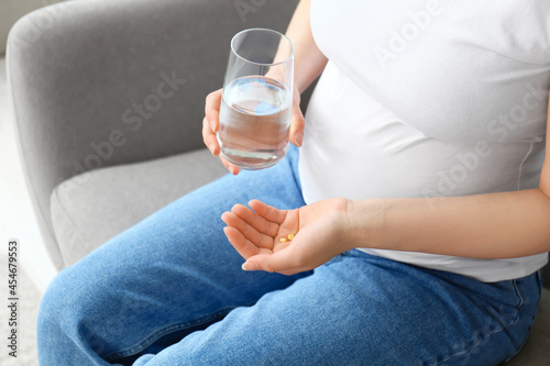 Young pregnant woman with pills and glass of water at home