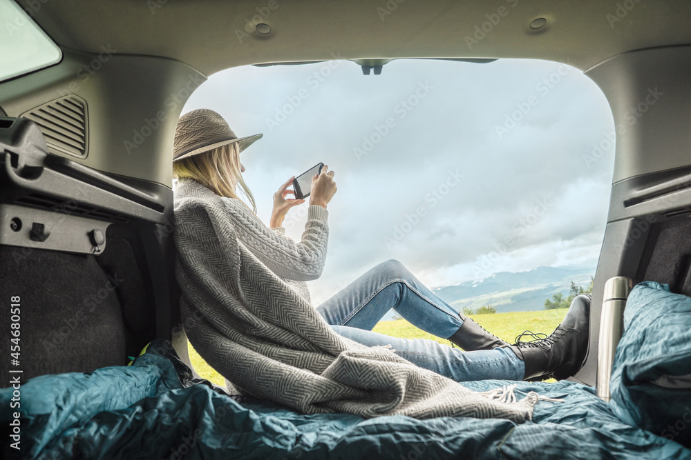 Girl resting in her car with her phone. Woman hiker, hiking backpacker  traveler camper in sleeping