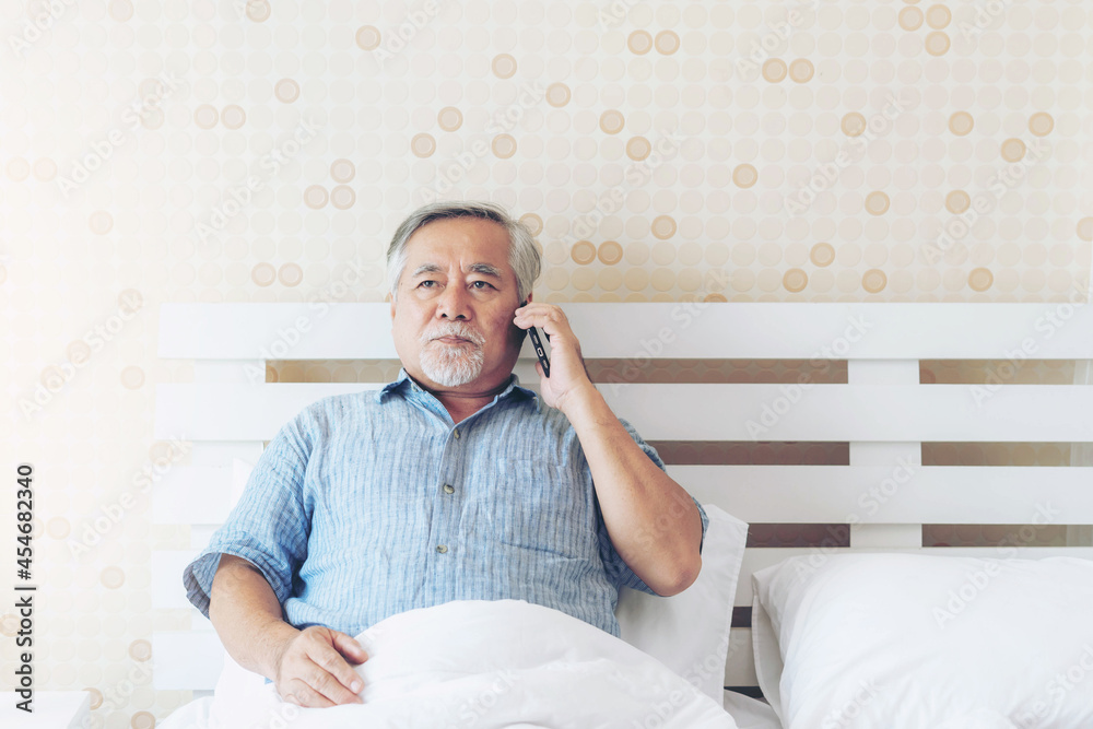 Fototapeta premium Senior Asian man , retired , old man make a call mobile phone on a bed in the bedroom , He was stressed , serious and worried - lifestyle senior at home concept