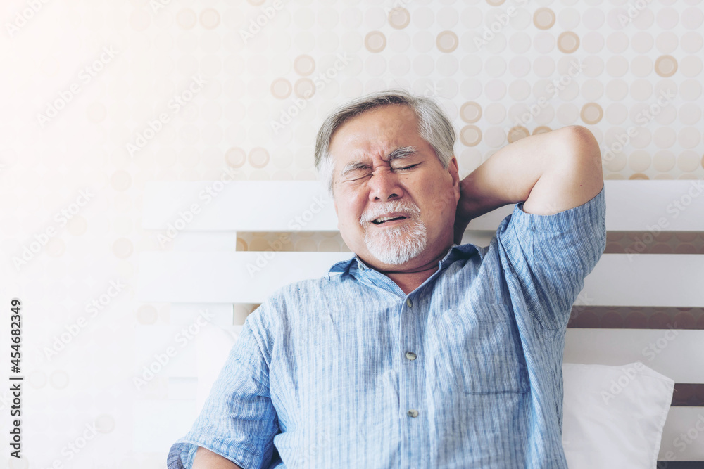 Obraz premium Senior Asian man , old man he wake up and sat on the bed , He had pain in the nape of his neck caused by sleeping on a pillow that is not correct posture - Senior people unhealthy diseased concept