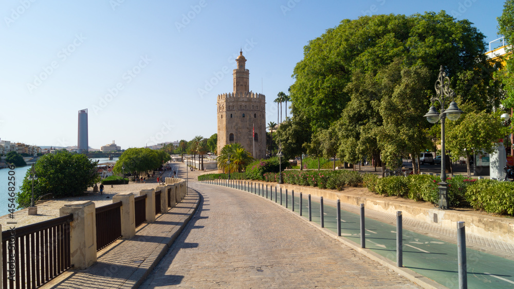 Promenade along the Guadalquivir river with views of the Torre del Oro (Tower of Gold or Golden Tower) in Seville (Andalusia, Spain). Urban landscape and emblematic place of the city.