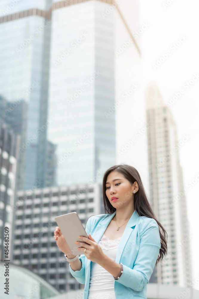 Fototapeta premium Beautiful cute girl wearing business woman clothes holding smart phone tablet computer on business district urban city background , business concept