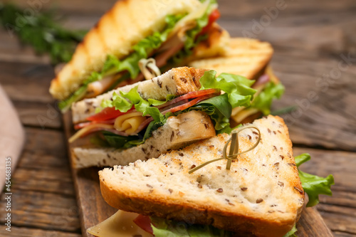 Board with tasty sandwiches on wooden background, closeup