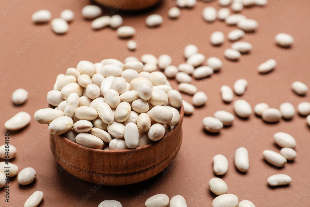 Bowl with raw beans on color background