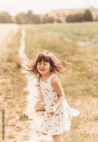 A little girl runs through a wheat field. The girl has fun and laughs with delight. Field with ripe ears of corn at sunset.