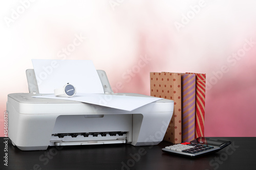 Compact home printer on desk with books against blurred background