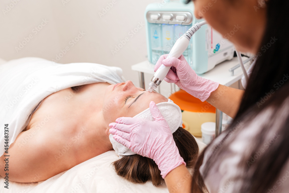 Beauty salon. The cosmetologist makes a aqua peeling procedure for the client. View from the shoulder. The concept of professional skin care Beauty salon. The cosmetologist makes a aqua peeling procedure for the client. View from the shoulder. The concept of professional skin care