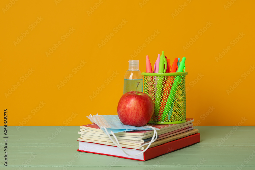 Stationery with apple and medical masks on table near color wall