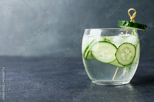 Glass of cold gin tonic and cucumber slices on dark background